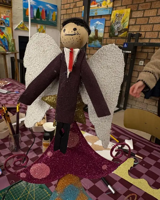 Een zelfgemaakt poppetje in pak met vleugels, op een roze vloerkleed.